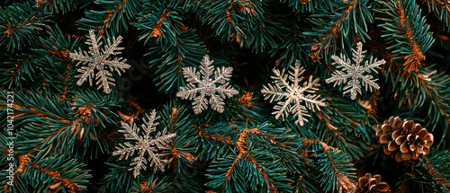 A close-up view of evergreen branches adorned with silver snowflakes and a pine cone, evoking a festive winter atmosphere.