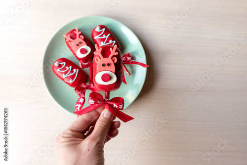 Flat lay of cake pops ice cream on a stick in red glaze with christmas picture on a plate background. Healthy homemade sweets. Party food. Top view.Healthy homemade sweets.