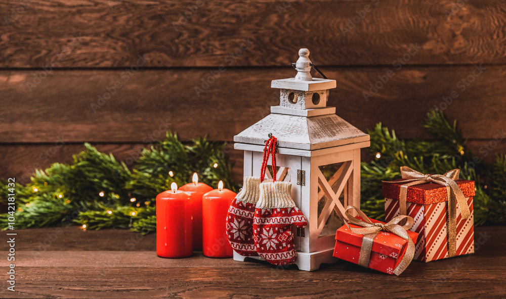 Merry Christmas greetings. Knitting mittens with ornaments, Lantern with candles, red candles and fir branches on a dark wooden background
