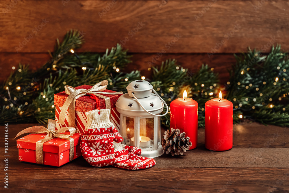 Merry Christmas greetings. Knitting mittens with ornaments, Lantern with candles, red candles and fir branches on a dark wooden background