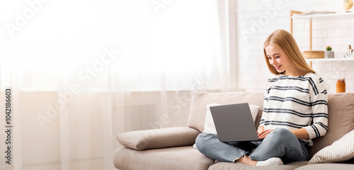 Looking for job. Student girl using laptop, sitting on couch, home interior, copy space