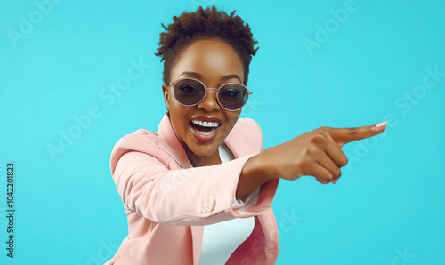 Portrait of happy confident young woman in stylish party outfit. Positive beautiful Afro American lady wearing fashionable pink suit and cool sunglasses looking at camera, smiling and pointing at you