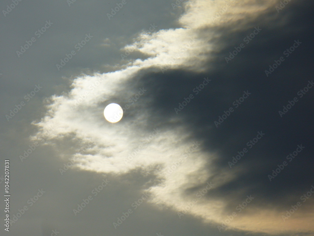 Cloudy sky with sun disc behind grey cloud - natural background. Topics: sun energy, weather change, cloud cover, meteorology, atmosphere, air space Cloudy sky with sun disc behind grey cloud - natural background. Topics: sun energy, weather change, cloud cover, meteorology, atmosphere, air space