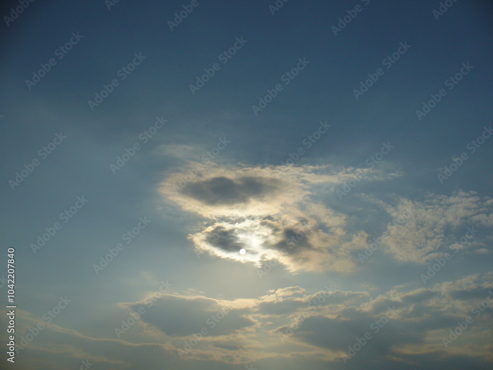 Obraz premium Blue sky with sun behind clouds with orange colors and sun rays - natural background. Topics: sun energy, weather, meteorology, atmosphere, air space
