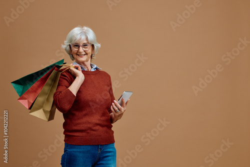 Happy senior woman with shopping bags and cell phone against neutral background looking at camera. photo