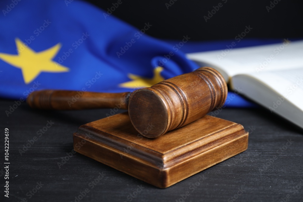 Judge's gavel, book and European Union flag on grey table against black background, closeup Judge's gavel, book and European Union flag on grey table against black background, closeup