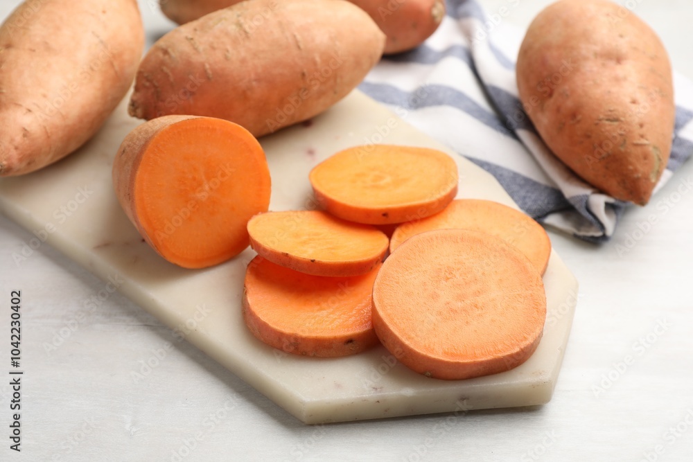 Fresh sweet potatoes and kitchen towel on white table, closeup Fresh sweet potatoes and kitchen towel on white table, closeup