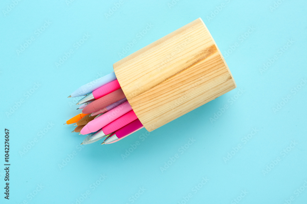 Fototapeta premium Wooden holder with different pens on blue background