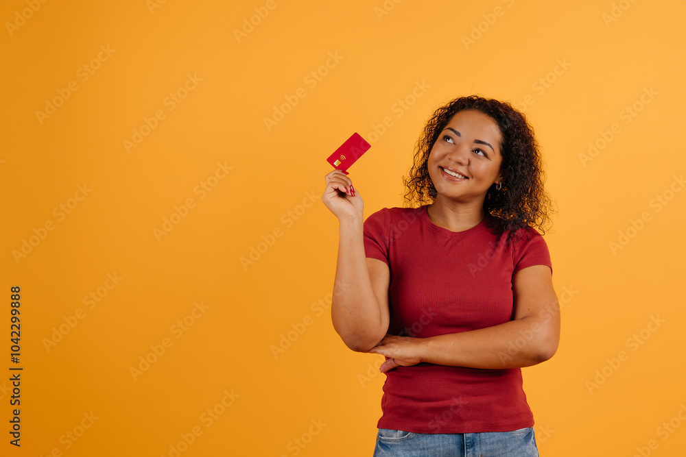 Time For Shopping. Pensive black lady holding credit card and looking away, planning what to buy, thoughtful african american woman standing over yellow studio background, copy space. High quality Time For Shopping. Pensive black lady holding credit card and looking away, planning what to buy, thoughtful african american woman standing over yellow studio background, copy space. High quality