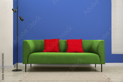 Photography Stylish green sofa with red pillows and lamp near blue wall indoors