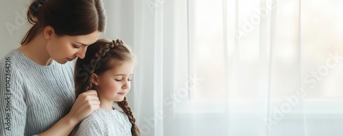 A mother braiding her daughter's hair by the window, with the morning light softly shining in