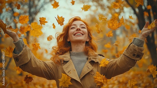 Woman with red hair, wearing a tan coat, joyfully throws autumn leaves in the air in a forest setting photo