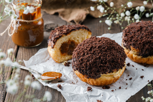 Set of cake donuts with chocolate and condensed milk on wooden background with flowers and cup of coffee. Sweets, dessert and pastry, top view, close up photo