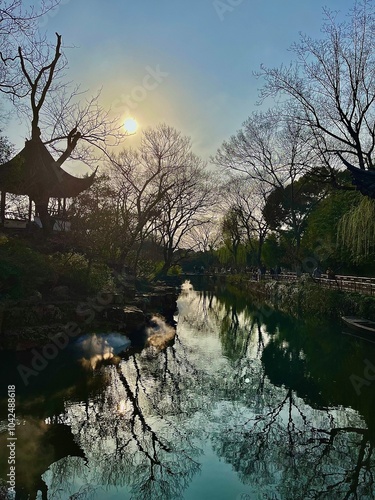 Tranquil River Scene with Reflections of Bare Trees and Setting Sun near a Traditional Pagoda