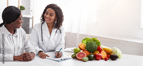 Friendly afro lady nutritionist making female patient anamnesis at clinic, discussing treatment, copy space