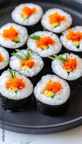 A plate of sushi rolls topped with orange fish roe and green garnishes.