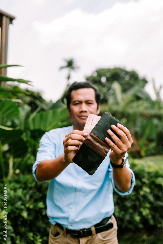 Fototapeta premium A Southeast Asian man is putting money into his wallet, focusing on the task. T