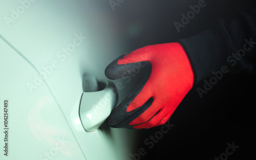 Man's gloved hand holding a screwdriver, attempting to pry open a car door handle. The image represents the concept of car theft, highlighting the risk and importance of vehicle security photo