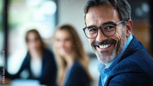 A smiling man in glasses engages with colleagues in a professional setting.