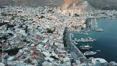 Greece,Kalimnos,Drone Footage high and above the harbor and the main town during sunset, sun is shinning on the steep hill of the town where the town is in shadow, lot of boats docked at the harbor. photo