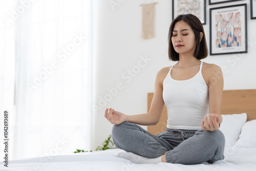 Beautiful asian women practicing yoga asana lotus position sitting on bed relax and stretch morning at home. Relaxation meditation wellness concept