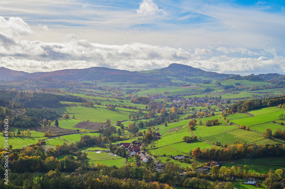 Obraz premium Autumn panoramic view of the beautiful landscape of the Hessian Rhön, with autumn forests, meadows and a small village near Hilders, autumn leaves, Hilders, Hesse, Germany 