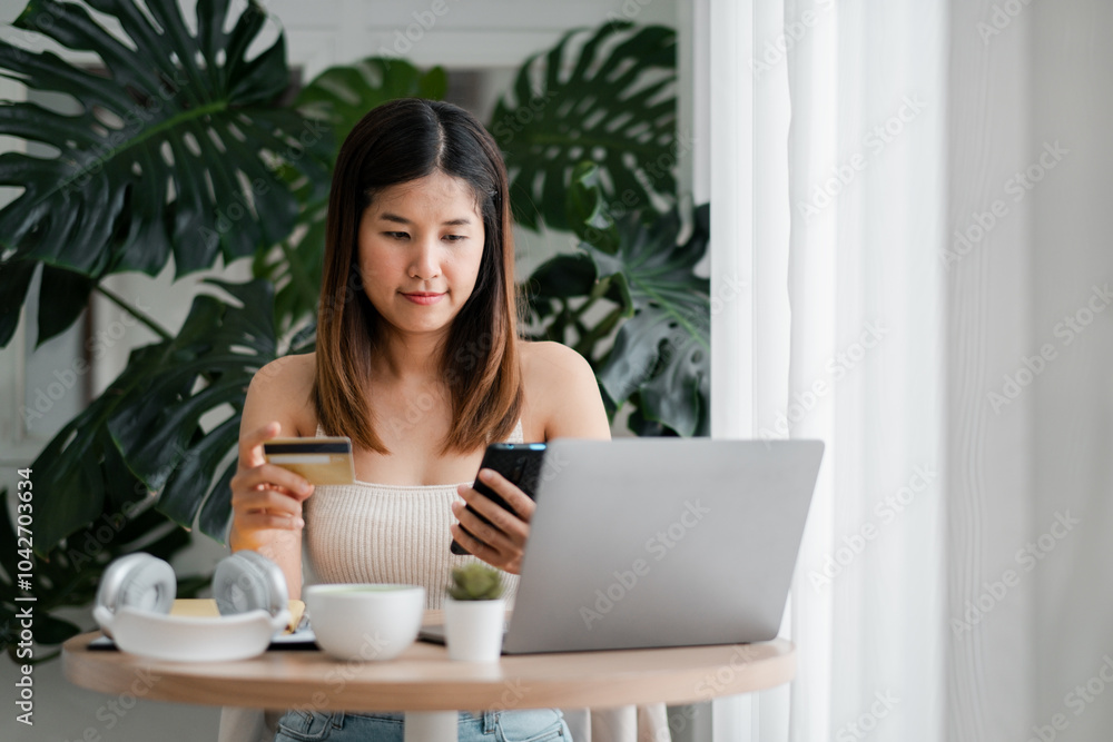 Woman using smartphone and credit card for online shopping at home, sitting by a laptop with headphones and coffee. Woman using smartphone and credit card for online shopping at home, sitting by a laptop with headphones and coffee.