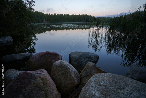 Serene lakeside view at dusk with large stones and lush greenery photo