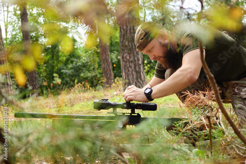 Man dressed in camouflage uniform in forest aiming his rifle as an athlete and hunter engaged in the action of hunting focusing on his target with precision and using military equipment photo