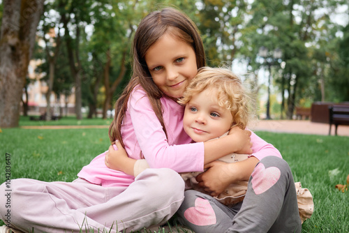 Cute Caucasian girl hugging her sibling in green park during springtime smiling and having fun in joyful moments of childhood playing outdoors together