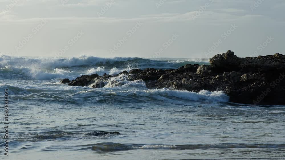 Waves roll gracefully past rocks near the shore, creating a soothing coastal scene. Waves roll gracefully past rocks near the shore, creating a soothing coastal scene.