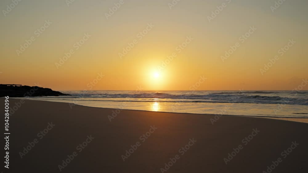 A wide shot captures waves crashing onto the beach, releasing a soft mist into the air, while the sun bathes the scene in a warm, golden glow. A wide shot captures waves crashing onto the beach, releasing a soft mist into the air, while the sun bathes the scene in a warm, golden glow.