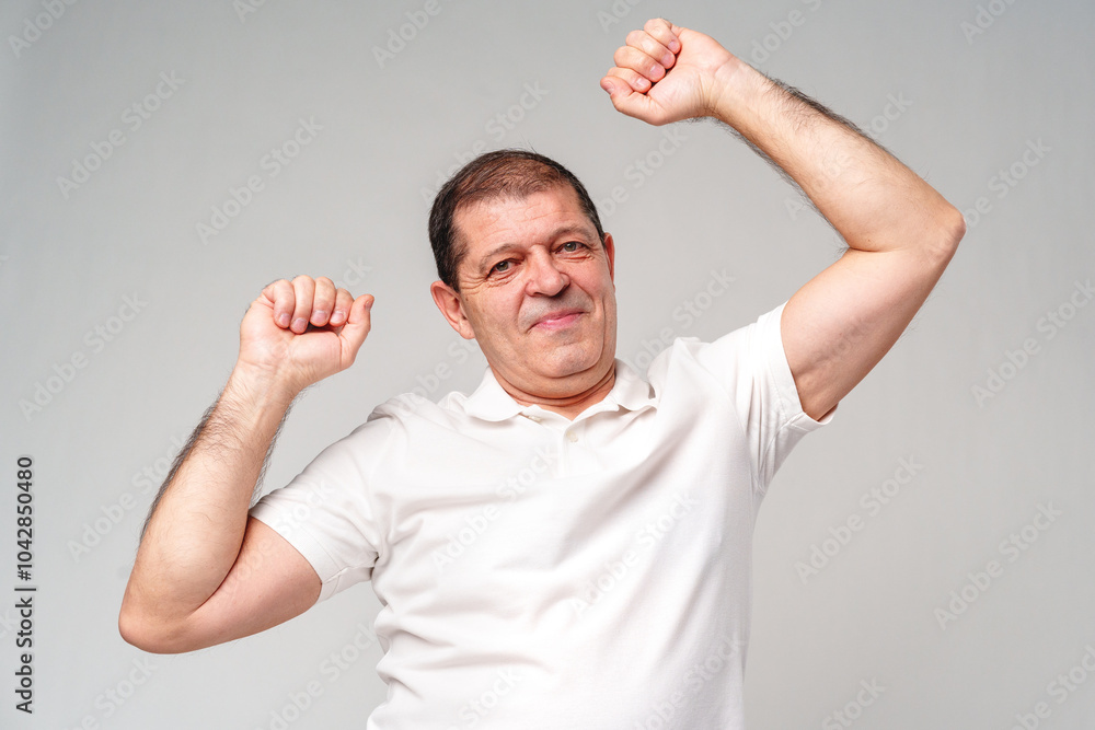 Fototapeta premium Happy older man showing off his strong biceps while standing against a light gray background