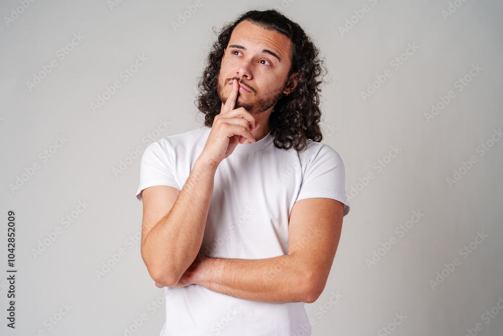 A man with curly hair thoughtfully pondering in a neutral background A man with curly hair thoughtfully pondering in a neutral background