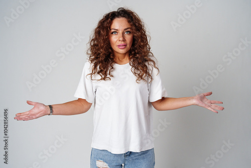 Cheerful woman with curly hair poses with open arms in a white shirt against a plain background photo