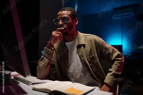 Fotografie Employee contemplating work in modern office, surrounded by open book, keyboard, and eyeglasses on desk