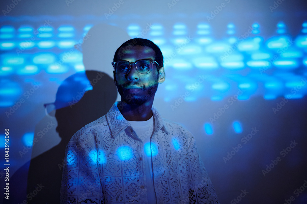 Portrait of man with glasses standing against a blue light effect background and wearing a lace-patterned shirt. Shadow creating an intriguing artistic double effect Portrait of man with glasses standing against a blue light effect background and wearing a lace-patterned shirt. Shadow creating an intriguing artistic double effect