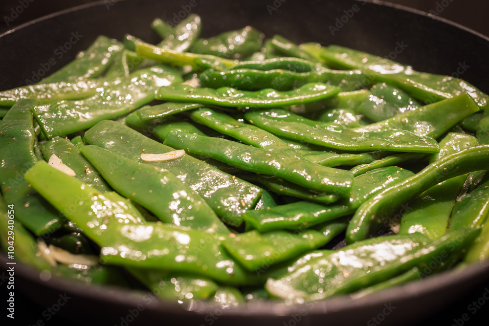 Flat Italian green beans are being sauteed in a pan with garlic and spices The bright green beans glisten with oil as they are cooked to serve as a flavorful side dish Flat Italian green beans are being sauteed in a pan with garlic and spices The bright green beans glisten with oil as they are cooked to serve as a flavorful side dish