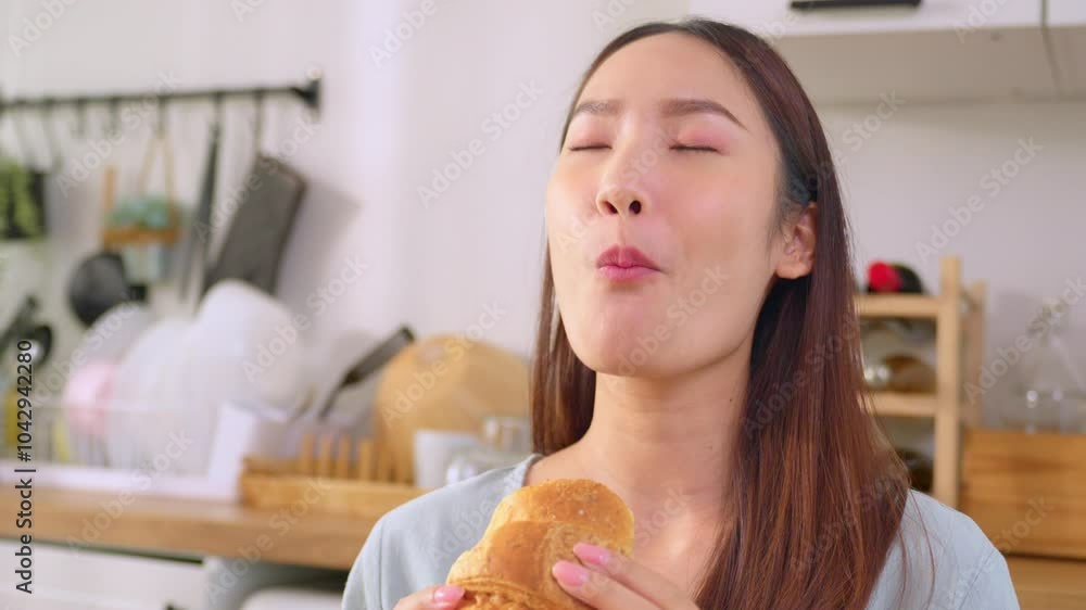 Asian attractive woman eating delicious croissant in kitchen at home. 