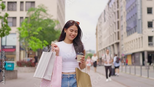 Mixed race woman hold shopping bags and drink while walk outdoors in city.  photo