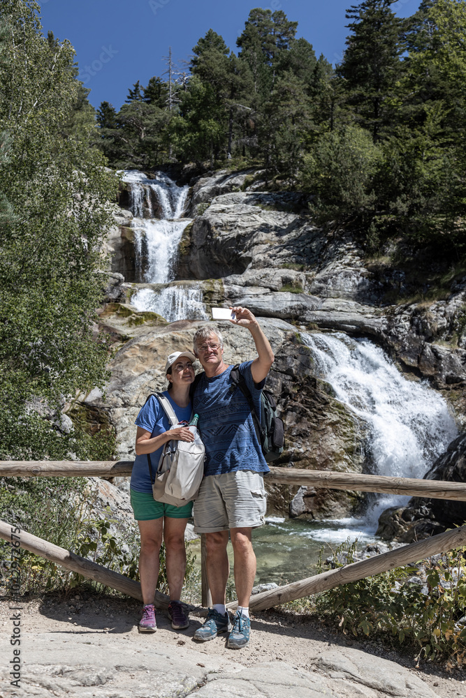 Backpacker middle old tourist couple taking photos of themselves in front of a waterfall in Spanish mountain. Backpacker middle old tourist couple taking photos of themselves in front of a waterfall in Spanish mountain.