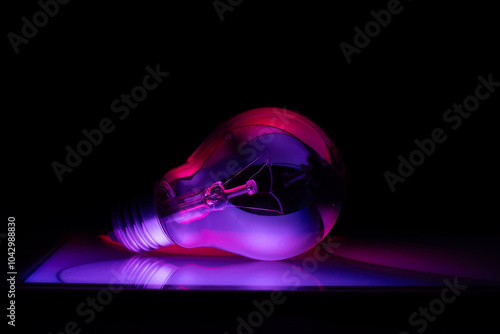 Light bulb on glass plate with reflections of colored lines  on black background