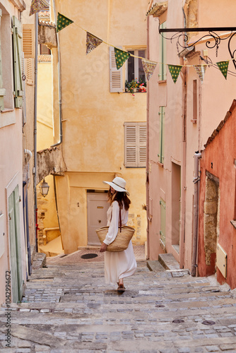 Rear view of woman wearing straw hat walking down alley at street photo