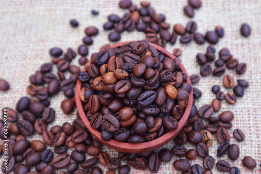 Fototapeta premium Robusta coffee beans or Coffea canephora in a wooden bowl and some scattered around it, close up view.