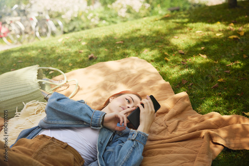 High angle view of young woman using phone while lying on mat in park photo