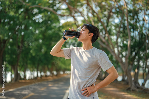 Fitness, Asian man in sportswear drinking water from a bottle during jogging exercise at public park. Healthy sports male from resting or on break after marathon or sprinting, wellness