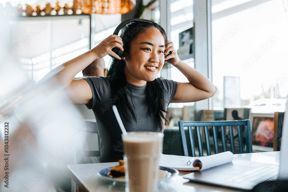Smiling young woman wearing headphones while sitting in cafe Smiling young woman wearing headphones while sitting in cafe