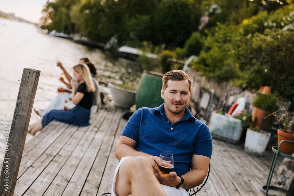 Portrait of mid adult man holding drink while sitting at jetty Portrait of mid adult man holding drink while sitting at jetty