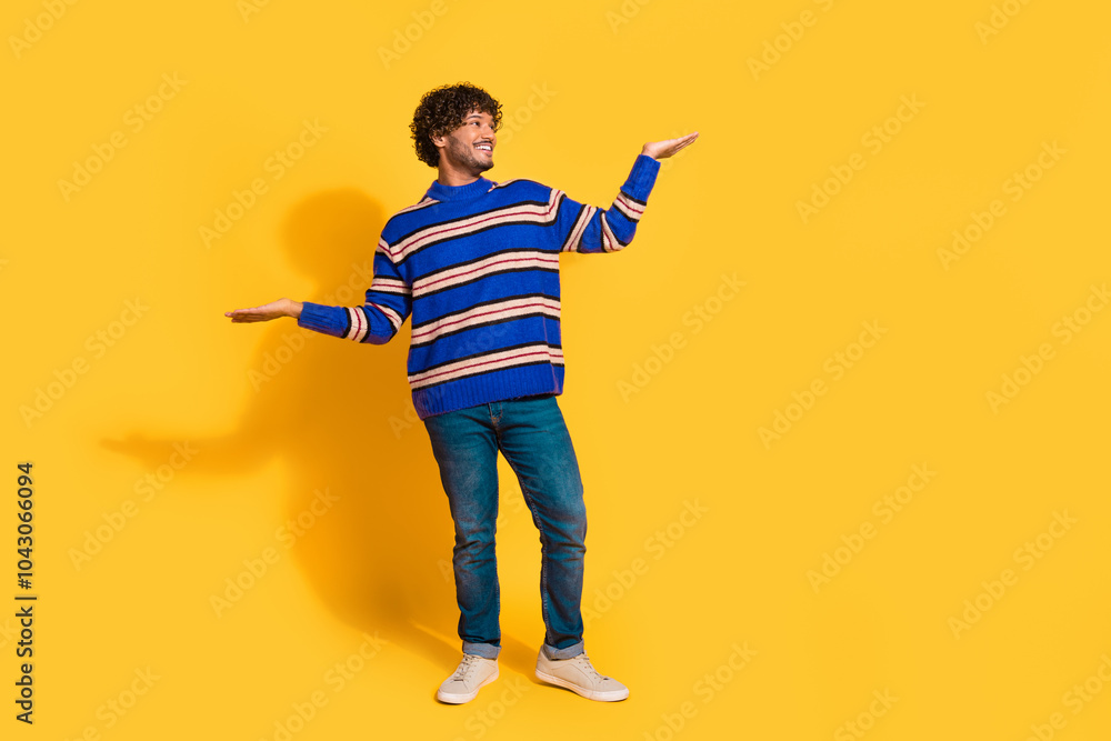 Full length photo of handsome young guy compare hold look empty space dressed blue striped garment isolated on yellow color background Full length photo of handsome young guy compare hold look empty space dressed blue striped garment isolated on yellow color background