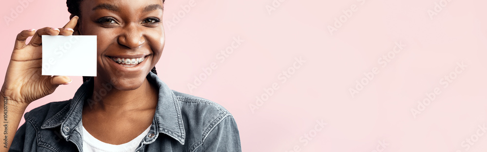 Orthodontics. African American Lady In Dental Braces Showing Orthodontist's Visiting Card Posing Over Pink Background. Mockup Orthodontics. African American Lady In Dental Braces Showing Orthodontist's Visiting Card Posing Over Pink Background. Mockup
